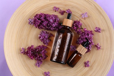 Photo of Tray with cosmetic products and lilac flowers on violet background, top view