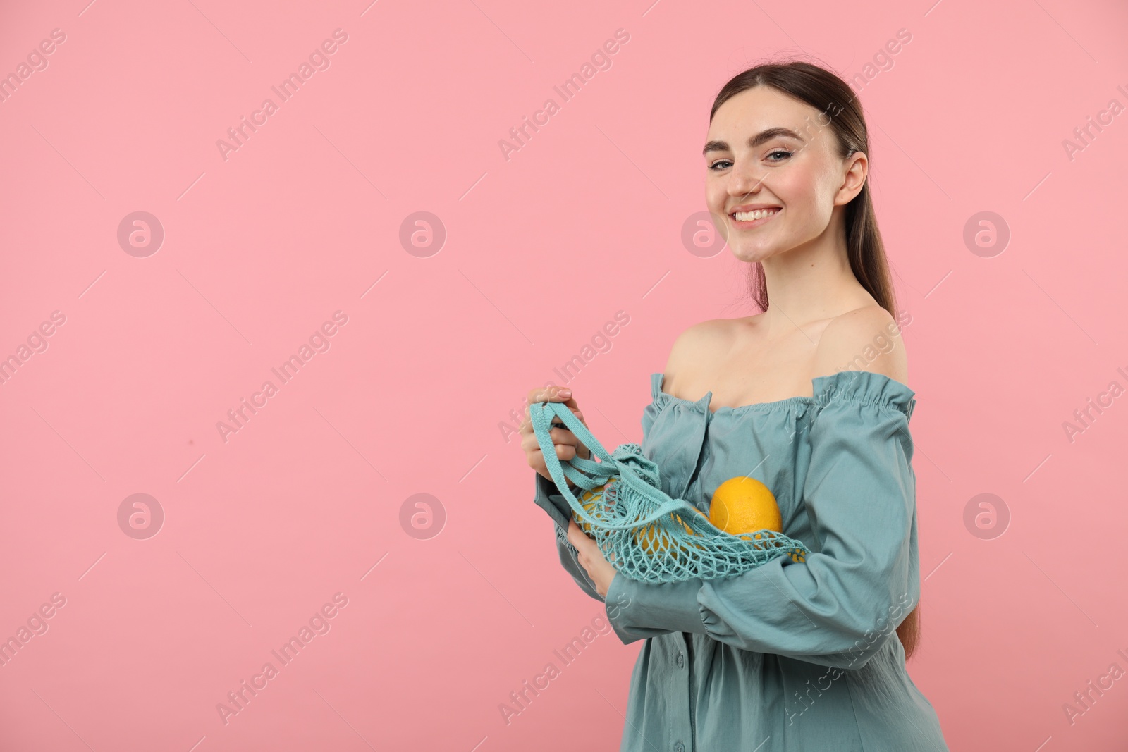 Photo of Woman with string bag of fresh lemons on pink background, space for text