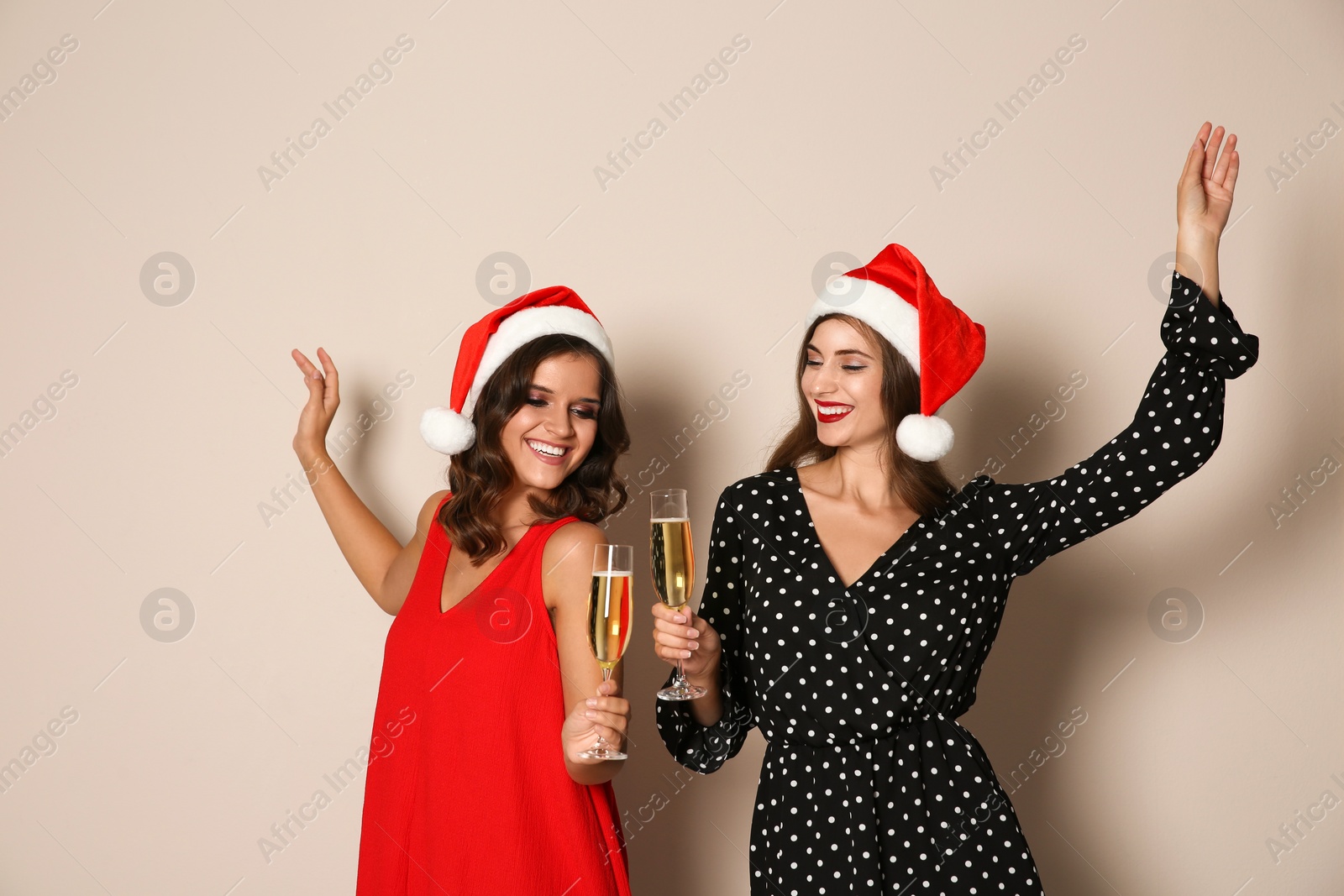 Photo of Happy women in Santa hats with champagne on beige background. Christmas party