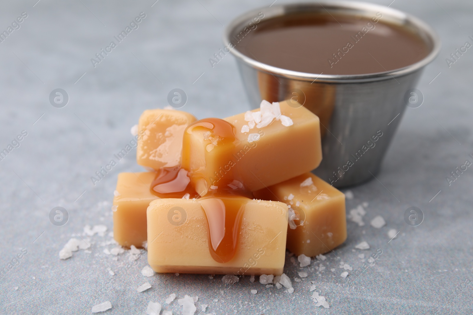 Photo of Yummy caramel candies, sauce and sea salt on grey table, closeup