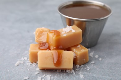 Yummy caramel candies, sauce and sea salt on grey table, closeup