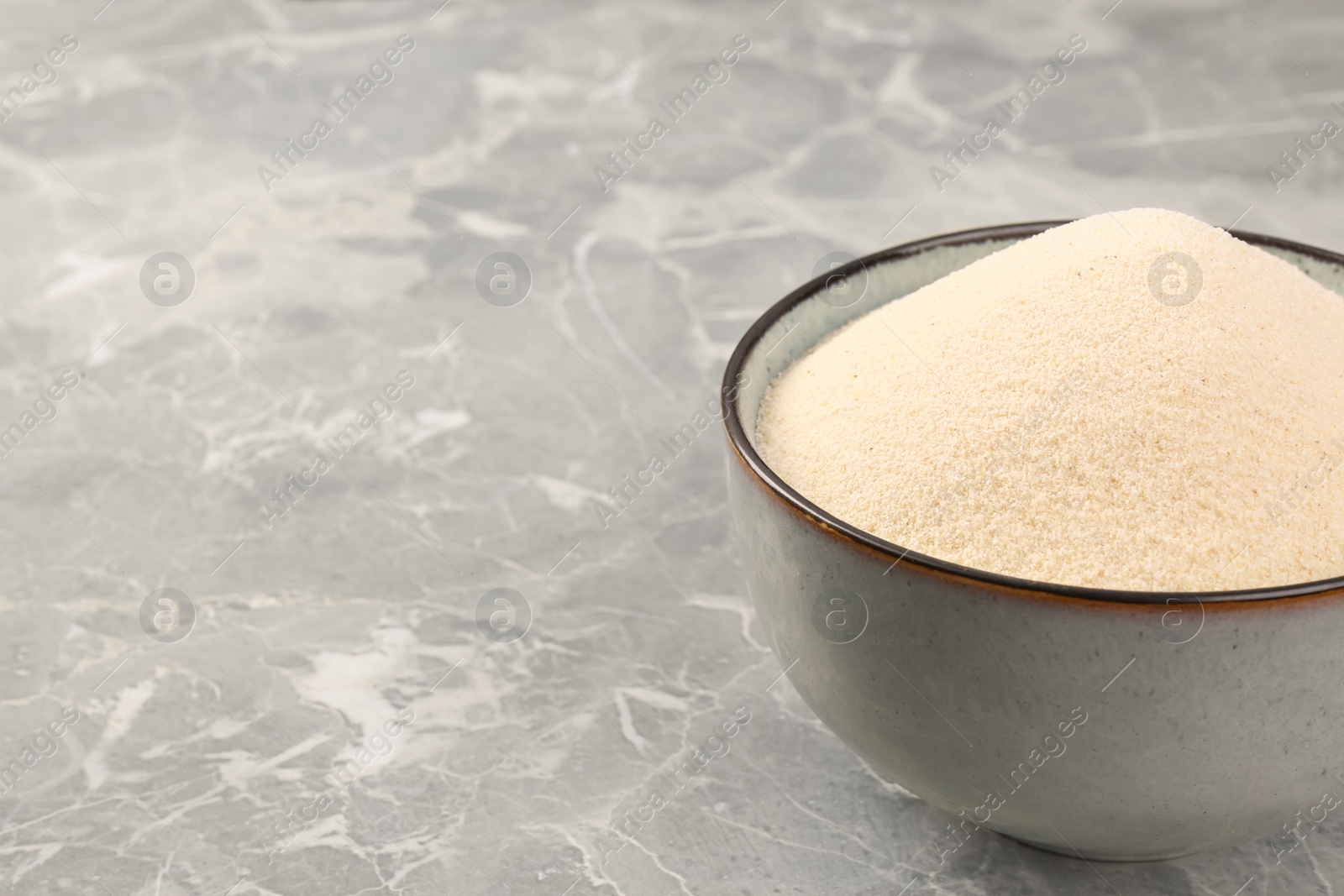 Photo of Uncooked organic semolina in bowl on grey table, closeup. Space for text