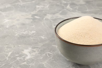 Photo of Uncooked organic semolina in bowl on grey table, closeup. Space for text