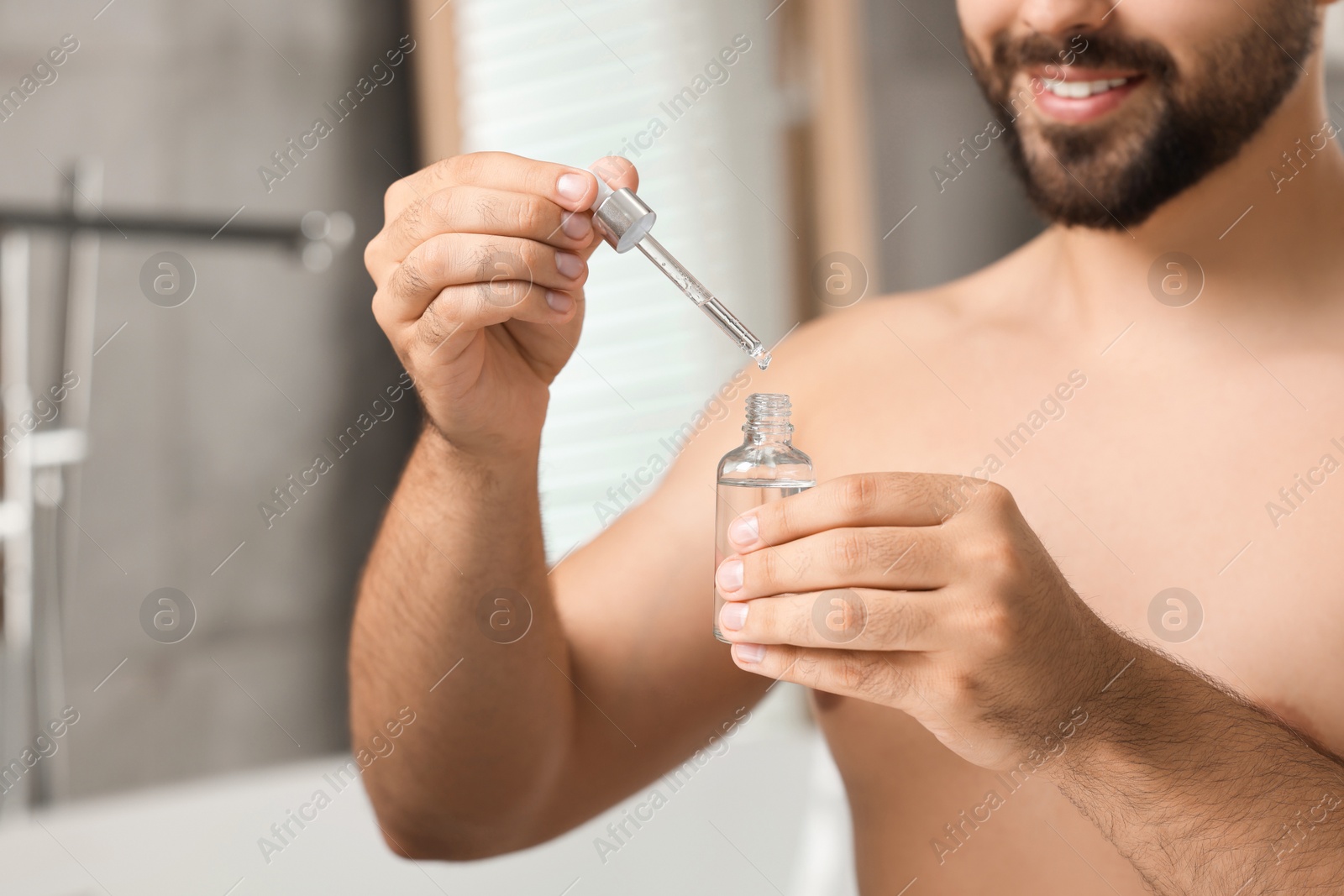 Photo of Young man with cosmetic serum in his hands in bathroom, closeup