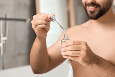 Photo of Young man with cosmetic serum in his hands in bathroom, closeup