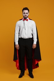 Photo of Man in scary vampire costume with fangs on orange background. Halloween celebration