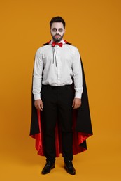 Man in scary vampire costume with fangs on orange background. Halloween celebration