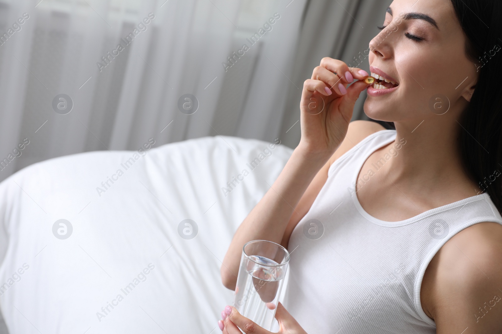 Photo of Woman with glass of water taking vitamin capsule in bedroom. Space for text