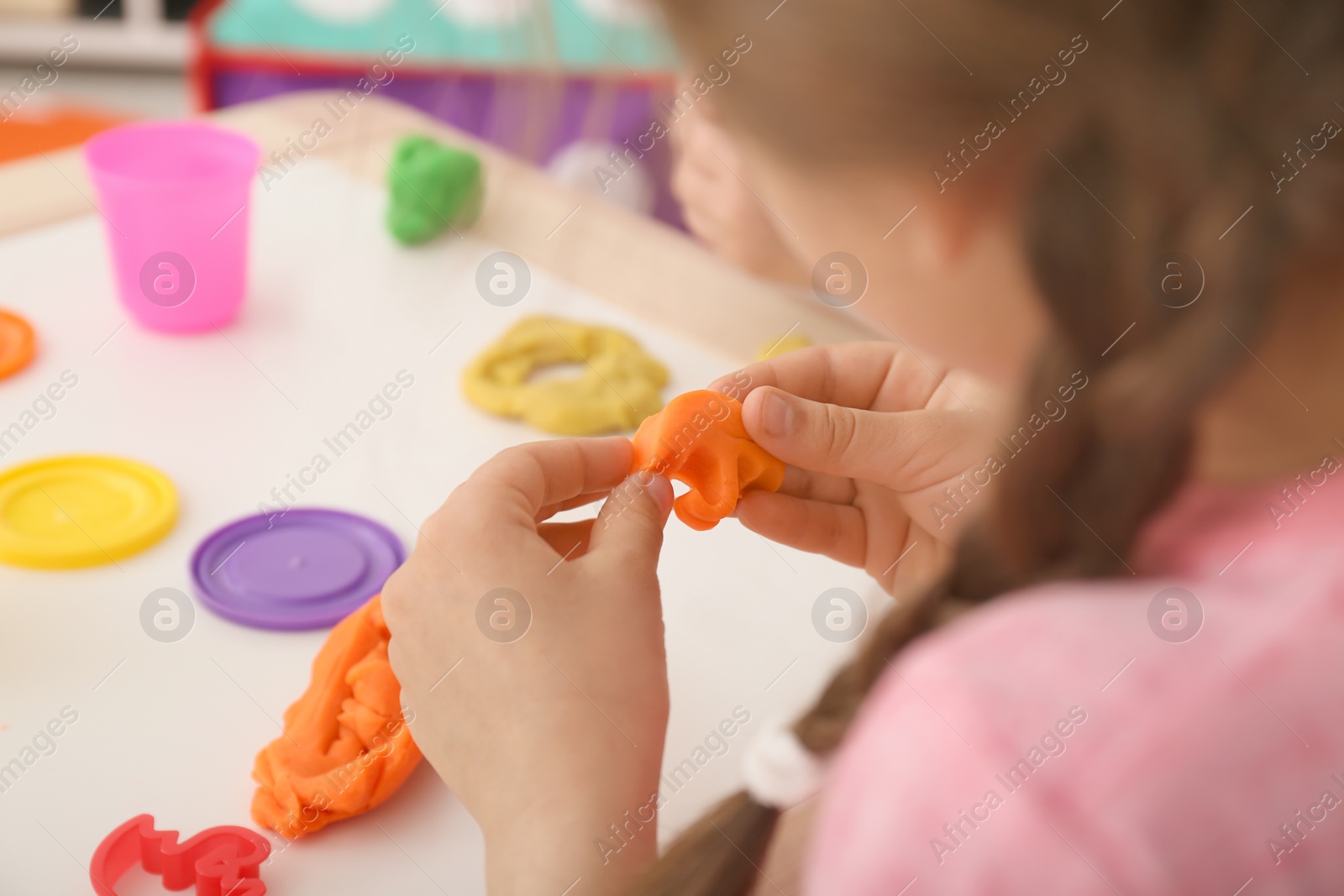 Photo of Cute little girl using play dough at table, closeup