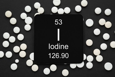 Photo of Card with iodine element and pills on black background, flat lay