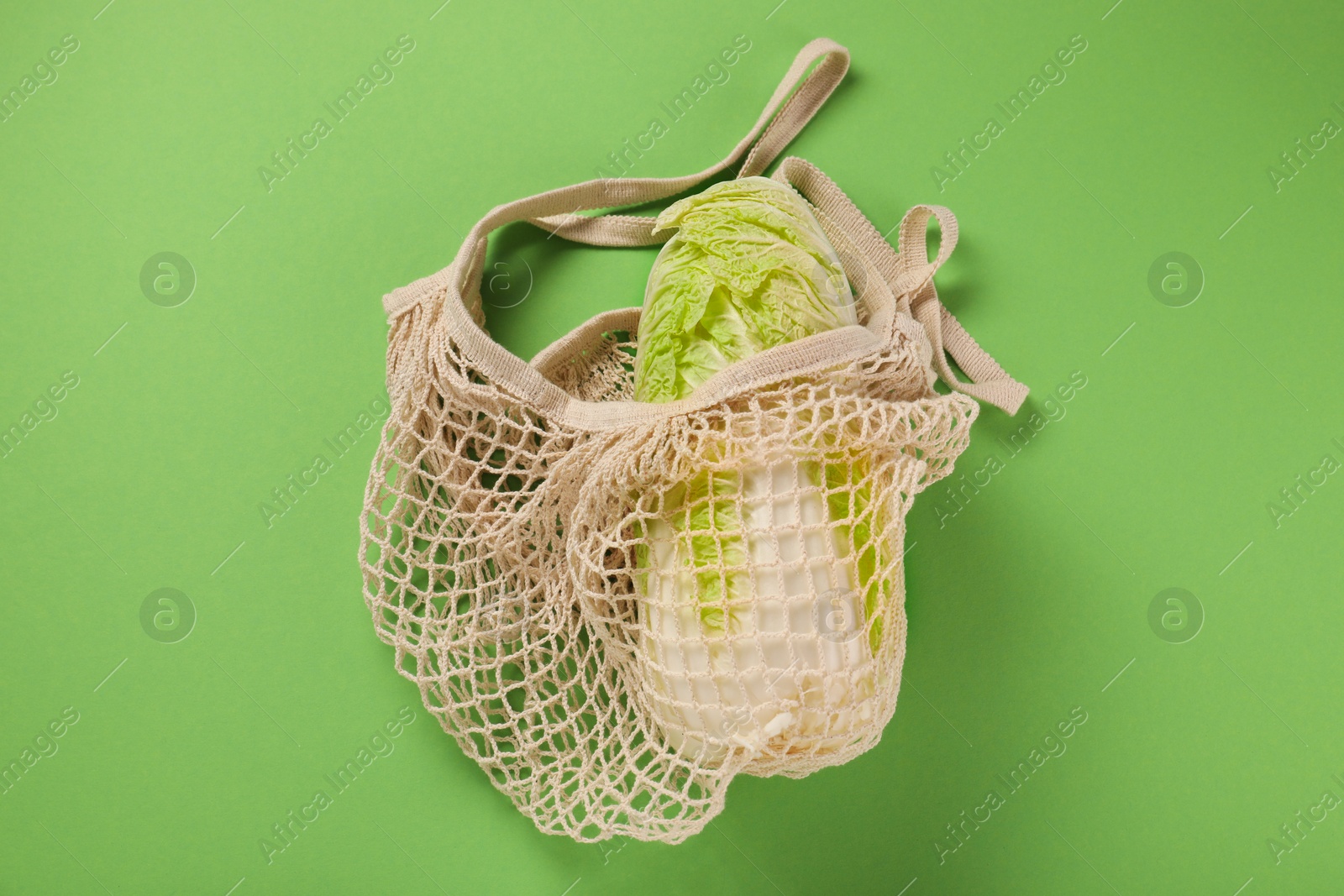 Photo of Fresh ripe Chinese cabbage in net bag on light green background, top view