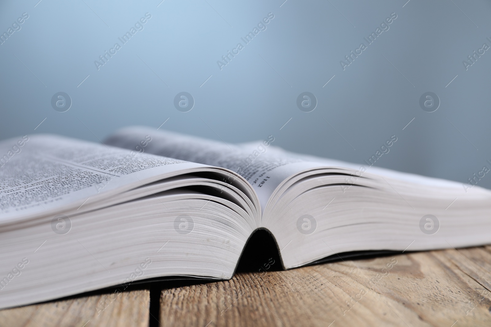 Photo of Closeup view of open Bible on wooden table against grey background. Religious book