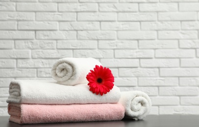 Photo of Rolled and folded soft towels with flower on table near brick wall. Space for text