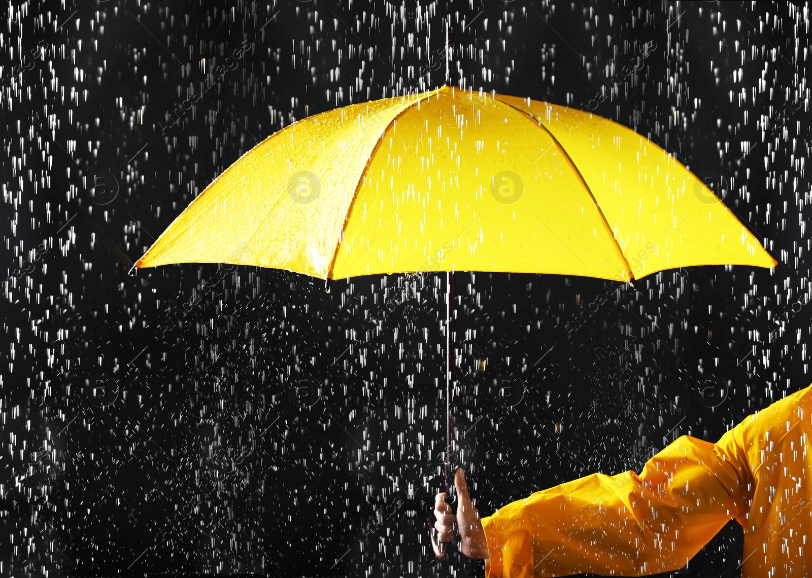 Photo of Woman holding bright umbrella under rain on dark background, closeup