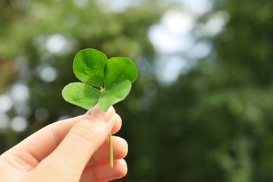 Photo of Woman holding four-leaf clover outdoors, closeup with space for text