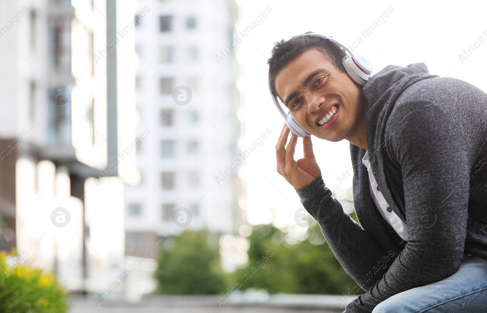 Photo of Handsome young African-American man with headphones listening to music on city street. Space for text