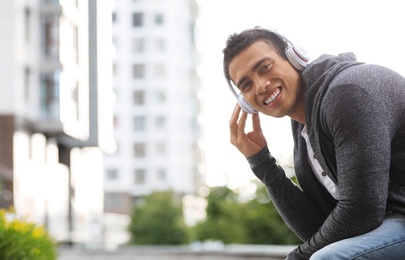 Handsome young African-American man with headphones listening to music on city street. Space for text