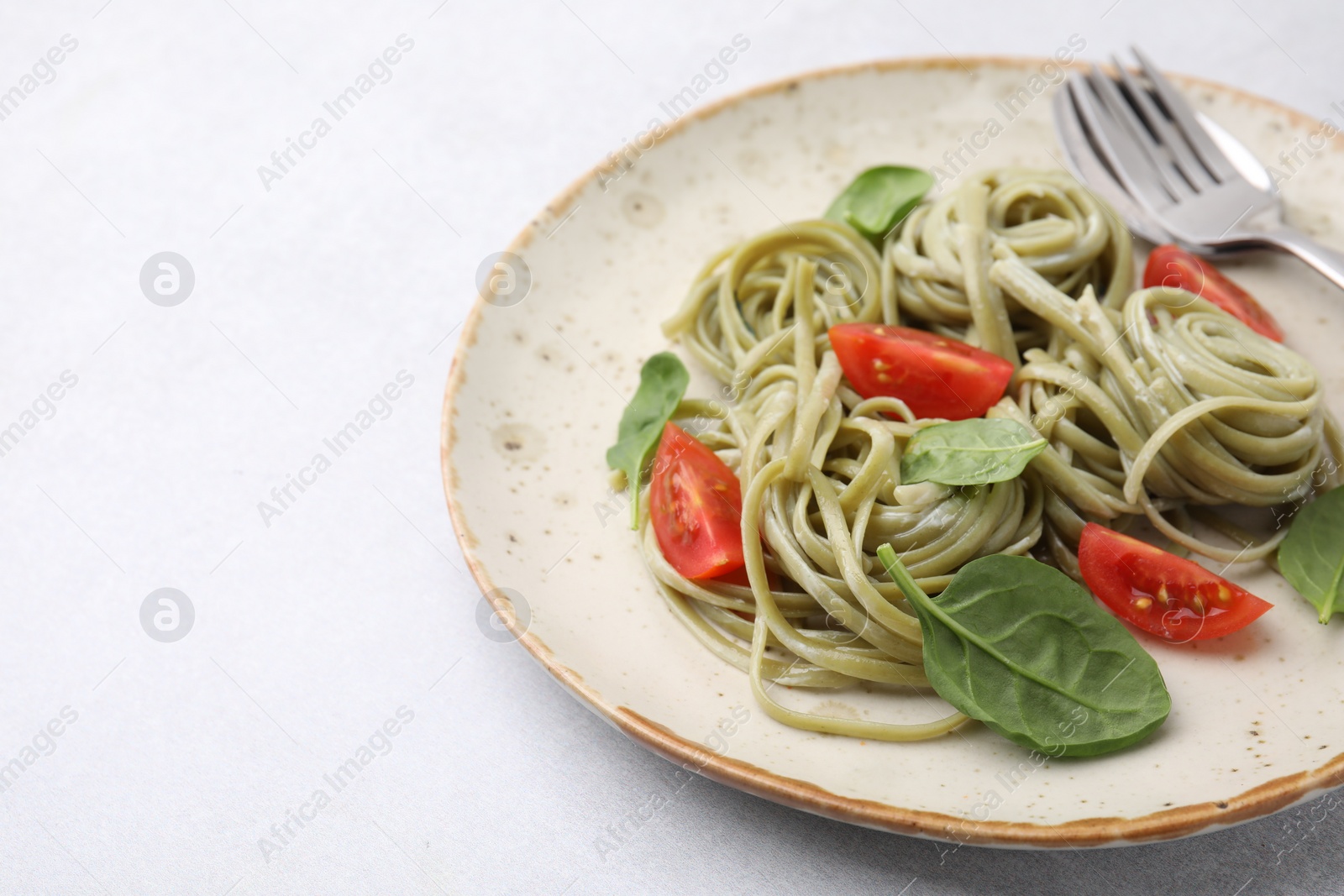 Photo of Tasty pasta with spinach, tomatoes and cutlery on light table, space for text