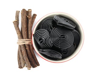 Tasty black candies and dried sticks of liquorice root on white background, top view