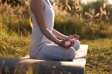 Photo of Woman practicing Padmasana on yoga mat outdoors, closeup with space for text. Lotus pose