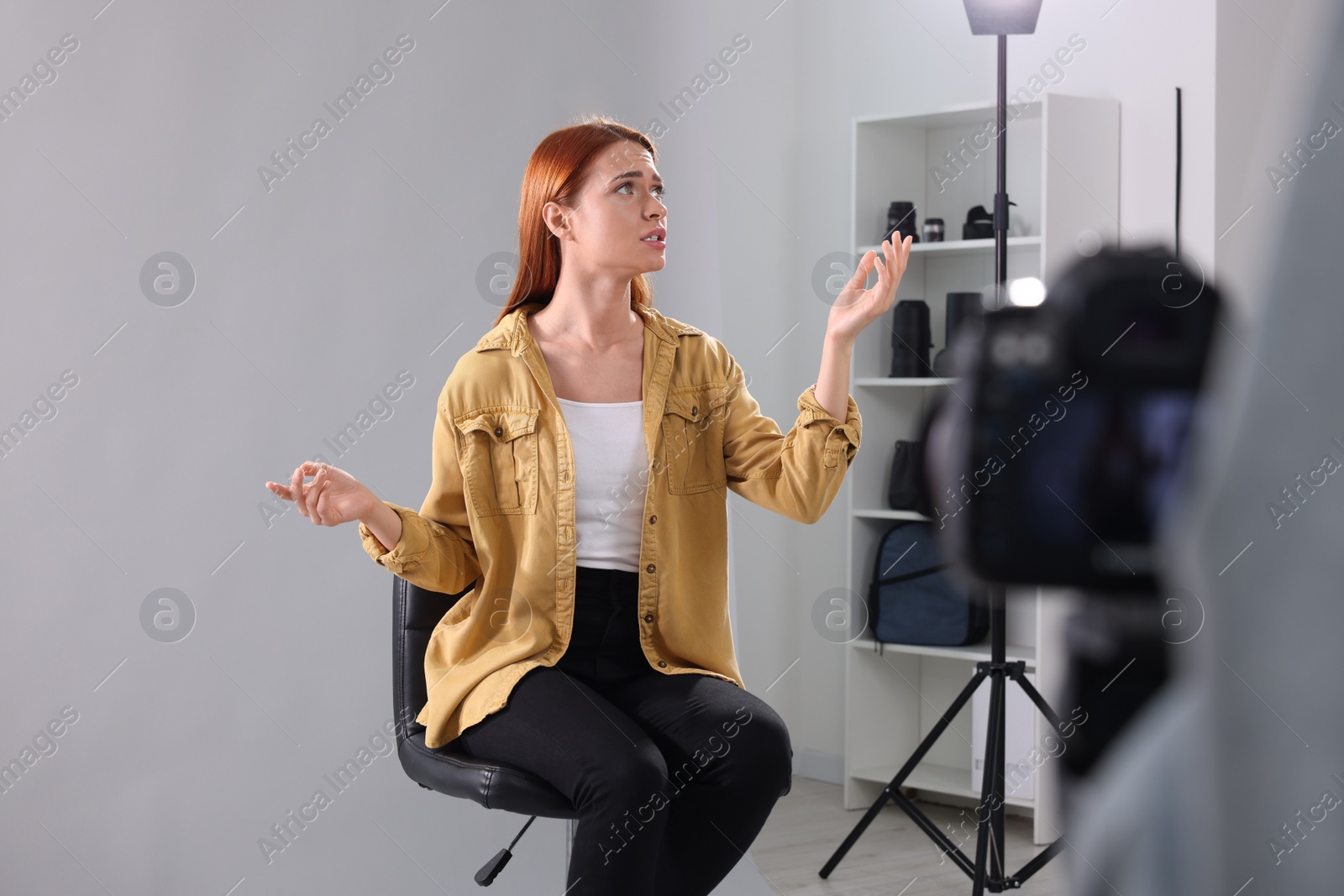 Photo of Casting call. Woman performing while camera operator filming her against light grey background in studio