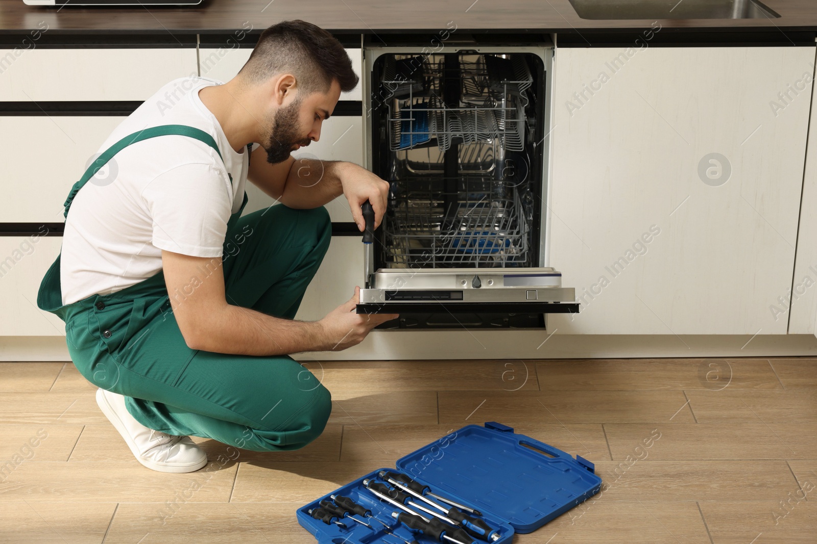 Photo of Serviceman repairing dishwasher door with screwdriver in kitchen