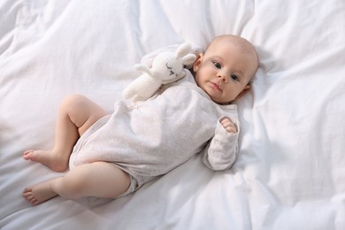 Photo of Cute little baby with toy lying on white sheets, top view