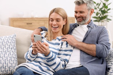 Photo of Happy affectionate couple using smartphone on sofa at home. Romantic date