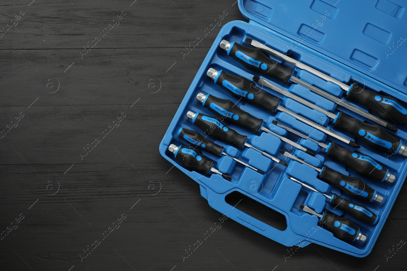 Photo of Set of screwdrivers in open toolbox on black wooden table, top view. Space for text