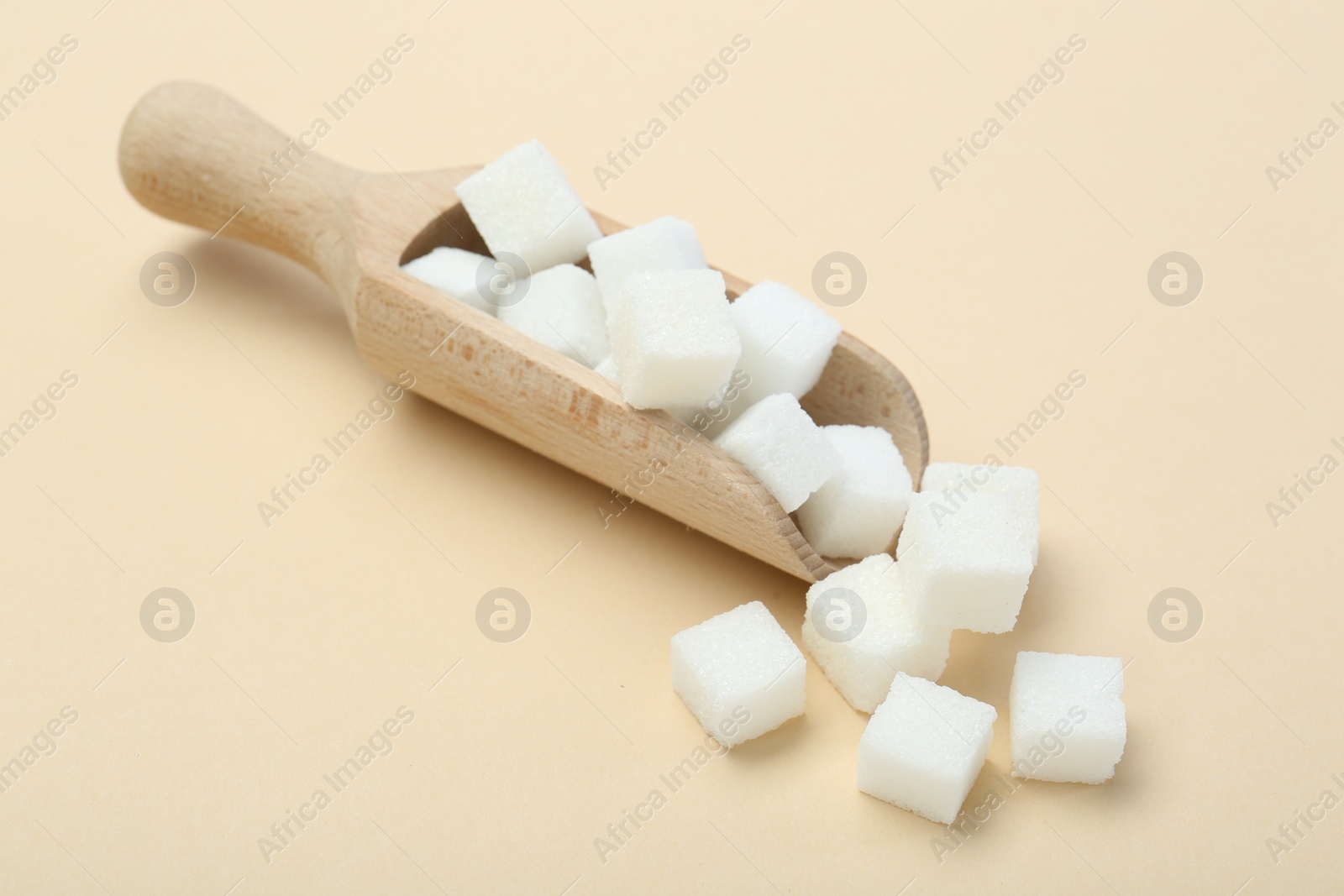 Photo of White sugar cubes and wooden scoop on beige background