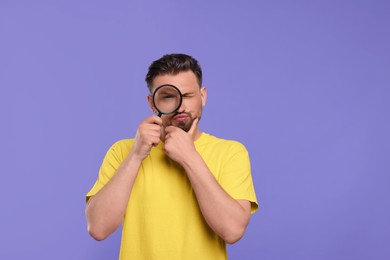 Photo of Handsome man looking through magnifier on violet background