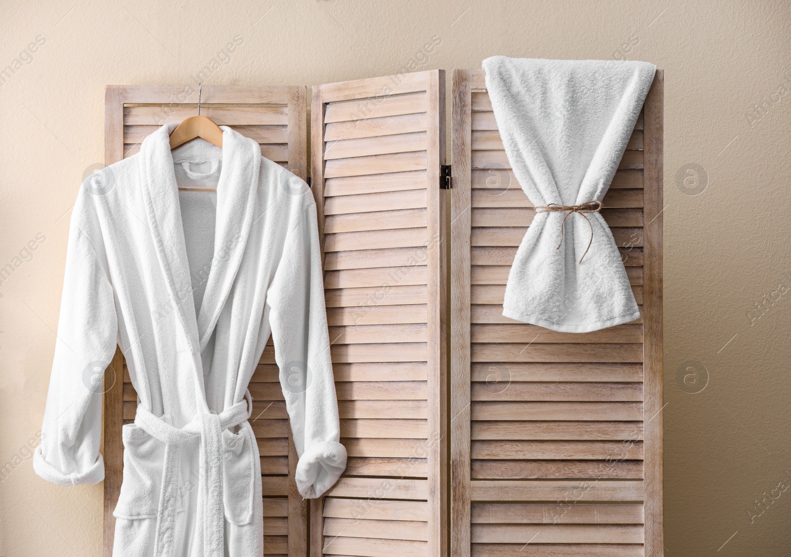 Photo of Soft comfortable bathrobe hanging on folding screen in stylish room interior