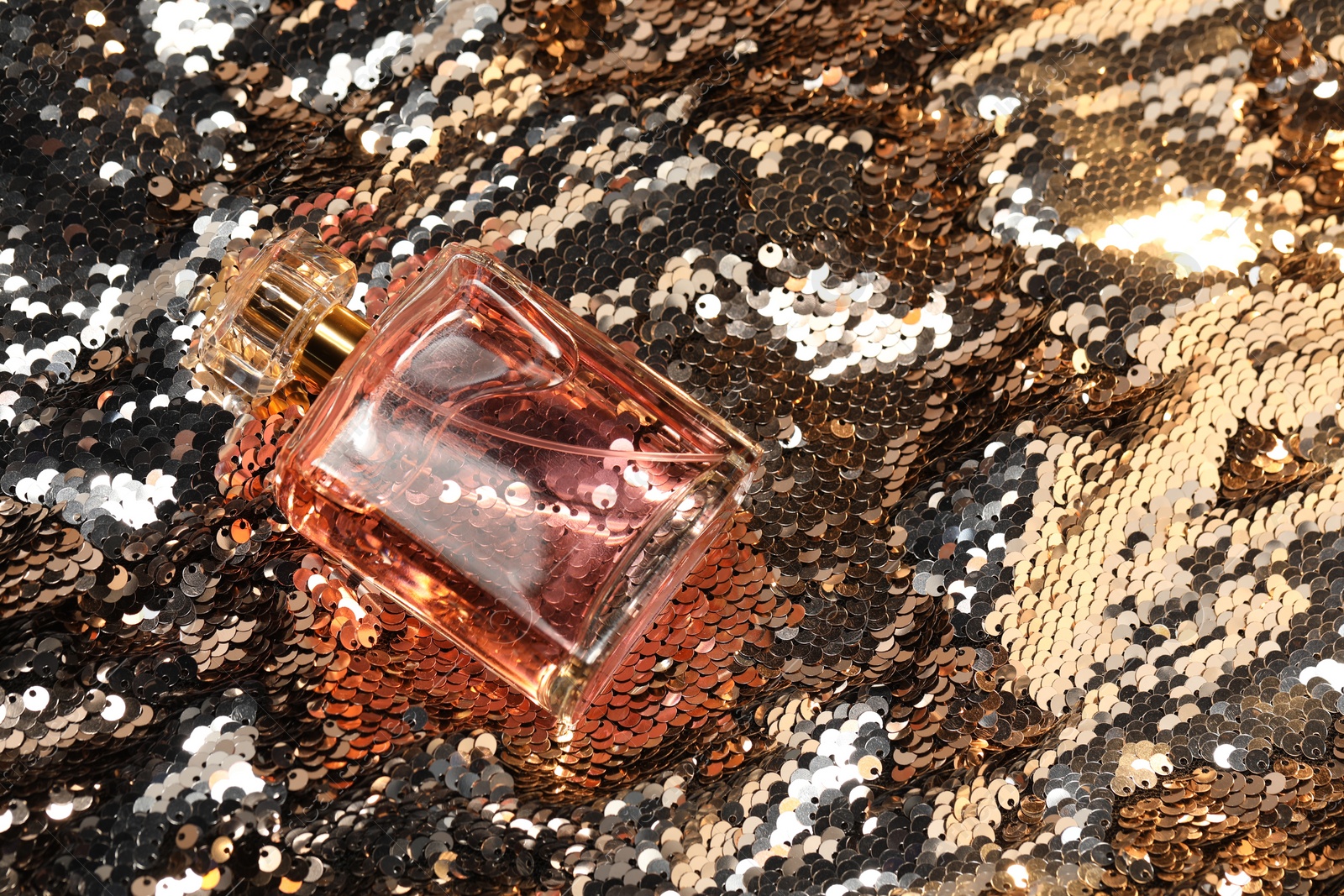 Photo of Luxury perfume in bottle on fabric with silver sequins, top view