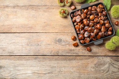 Photo of Delicious roasted edible chestnuts on wooden table, flat lay. Space for text