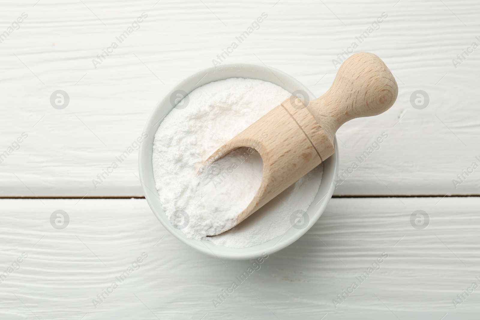 Photo of Baking powder in bowl and scoop on white wooden table, top view