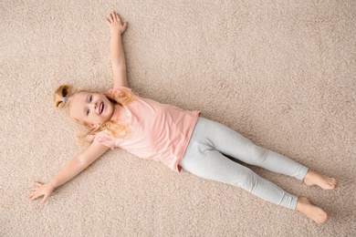 Cute little girl lying on cozy carpet at home, top view