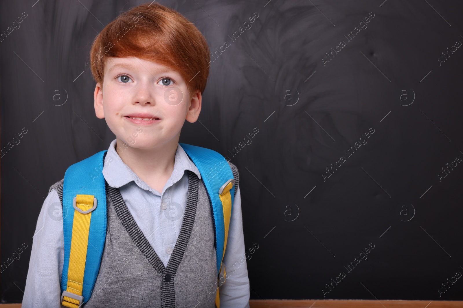 Photo of Smiling schoolboy near blackboard. Space for text