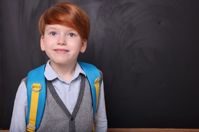 Photo of Smiling schoolboy near blackboard. Space for text