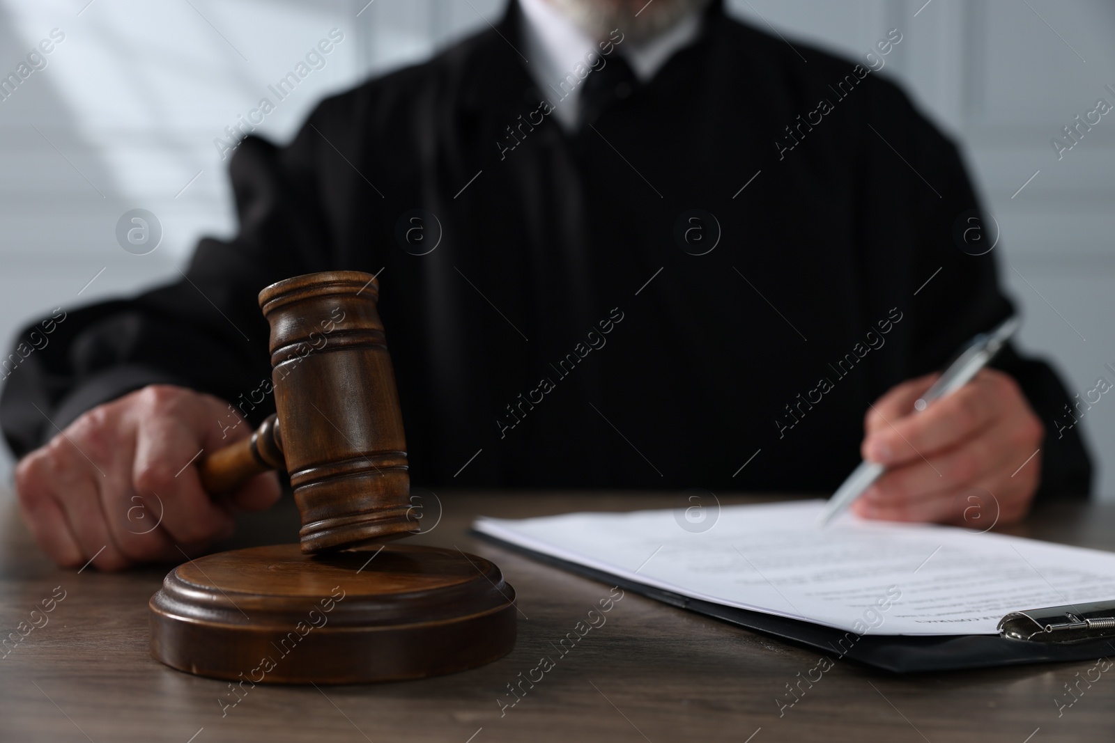 Photo of Judge with gavel and papers sitting at wooden table, closeup