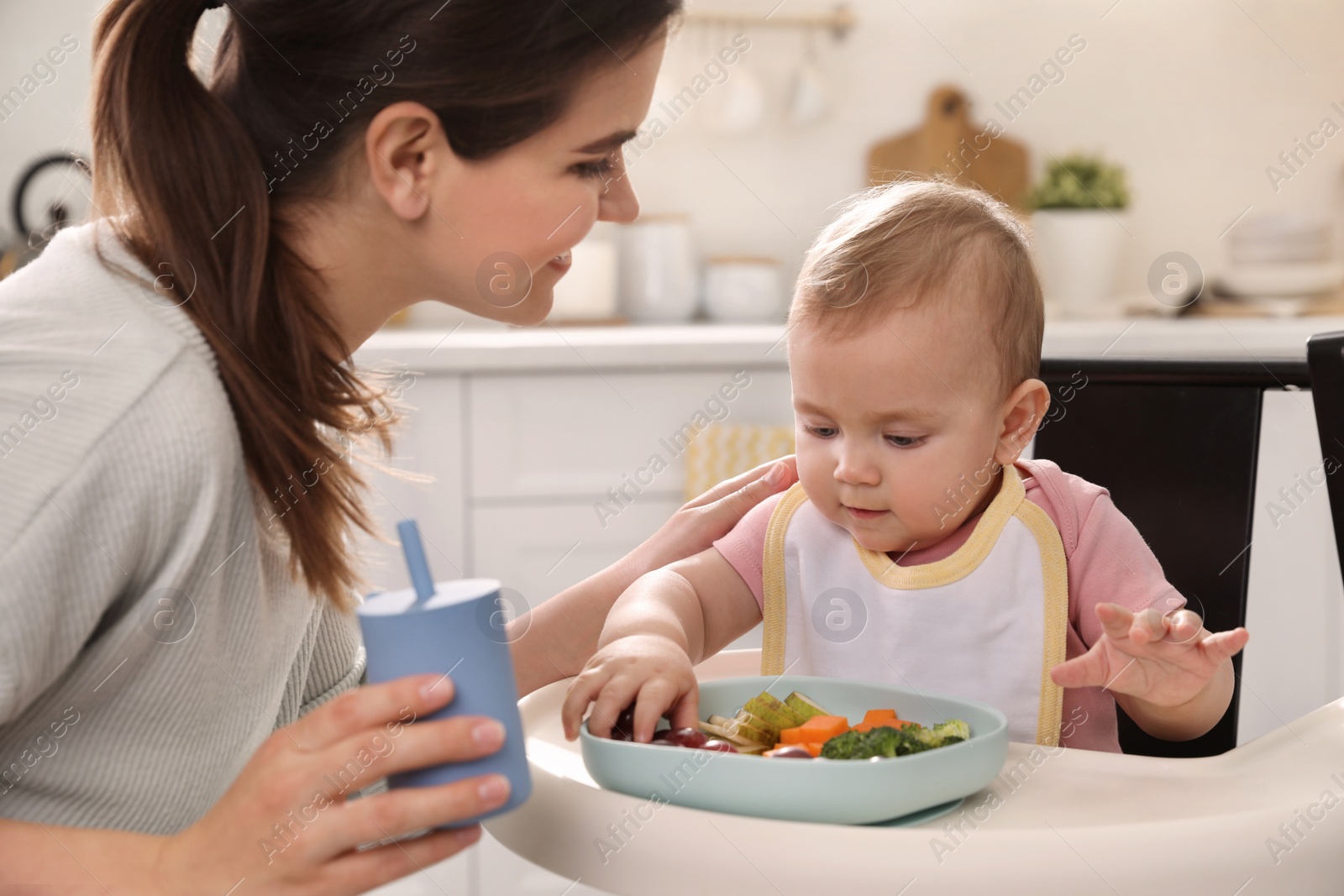 Photo of Mother feeding her cute little baby in kitchen