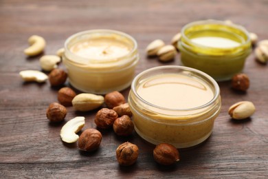 Different types of delicious nut butters and ingredients on wooden table, closeup