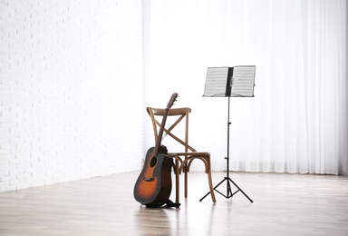 Photo of Acoustic guitar, chair and note stand with music sheets indoors