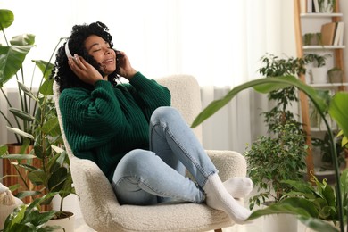 Photo of Relaxing atmosphere. Happy woman wearing headphones and listening music in room with beautiful houseplants