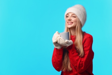 Photo of Portrait of emotional young woman in stylish hat, sweater and mittens with cup on color background, space for text. Winter atmosphere