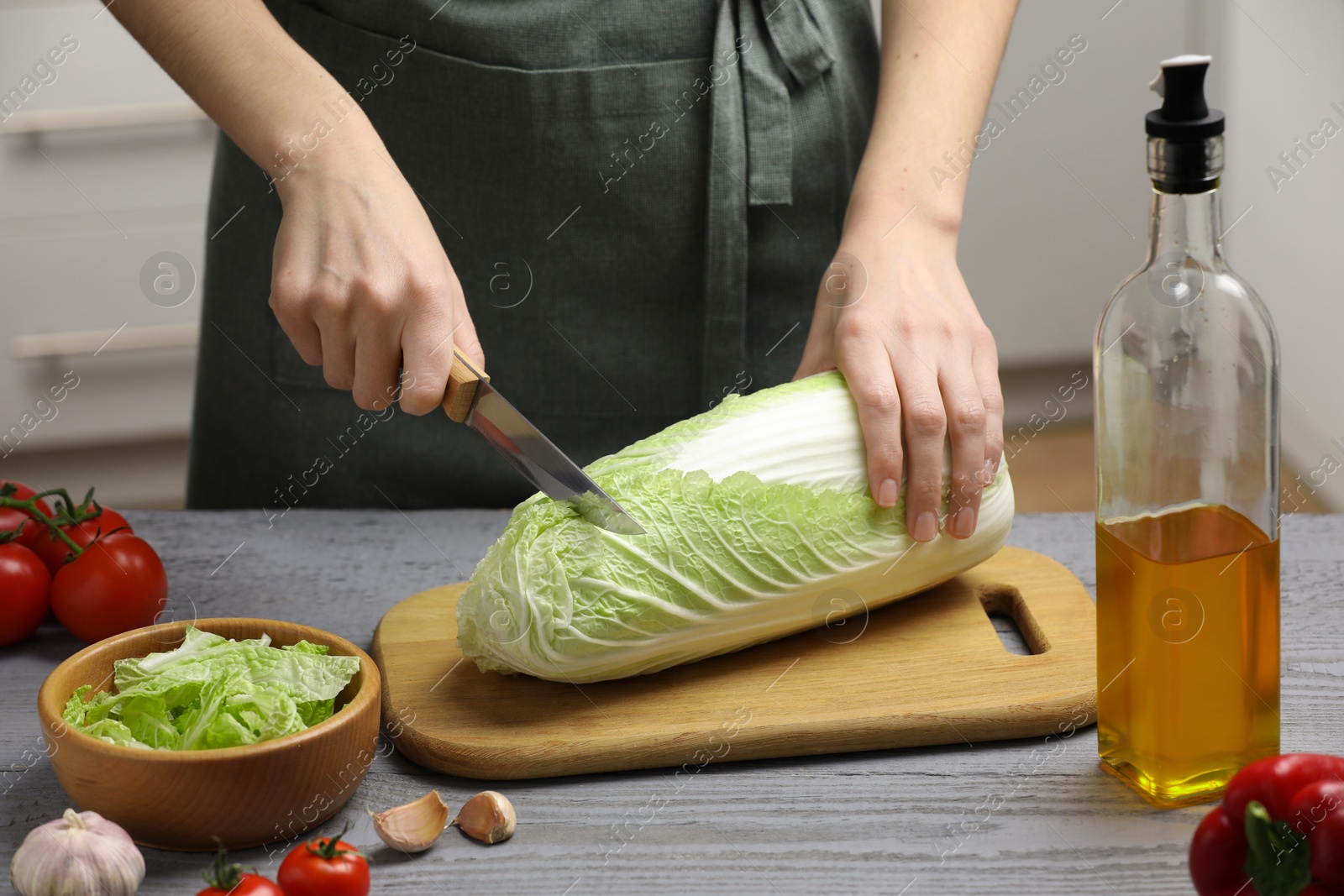 Photo of Woman cutting fresh chinese cabbage at grey wooden table in kitchen, closeup