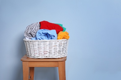 Photo of Laundry basket with dirty clothes on stool against color background