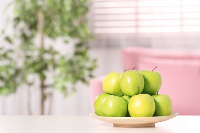 Plate with sweet green apples on table in room, space for text