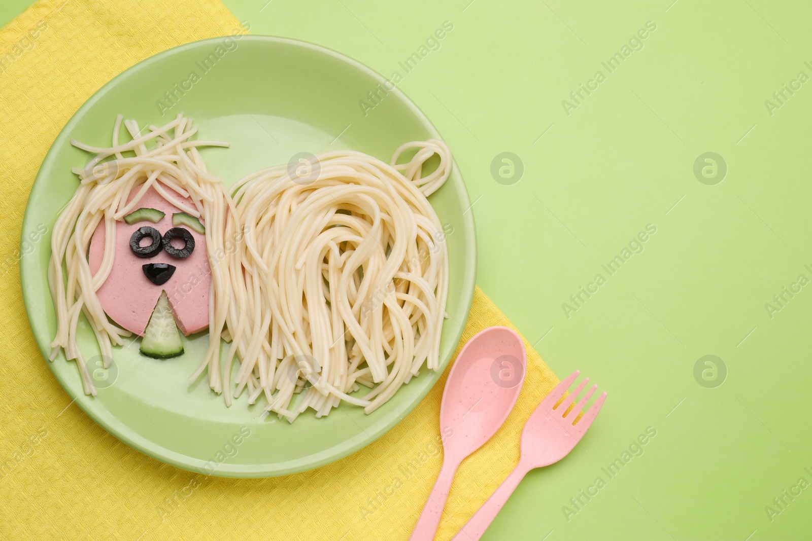 Photo of Creative serving for kids. Plate with cute dog made of tasty pasta, sausage and cucumber on green table, flat lay. Space for text