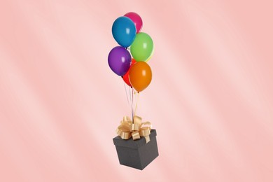 Many balloons tied to gift box on pink background