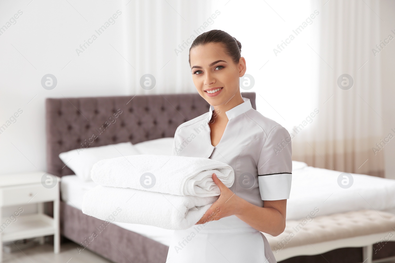 Photo of Young chambermaid with clean towels in bedroom